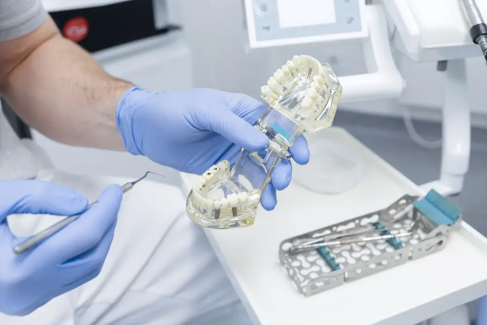 Dentist in blue gloves holding a white dental model and tool for complex tooth replacement planning