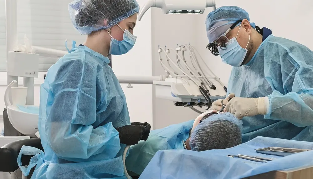 Two dentists in blue scrubs, masks, and hairnets performing a full mouth reconstruction procedure