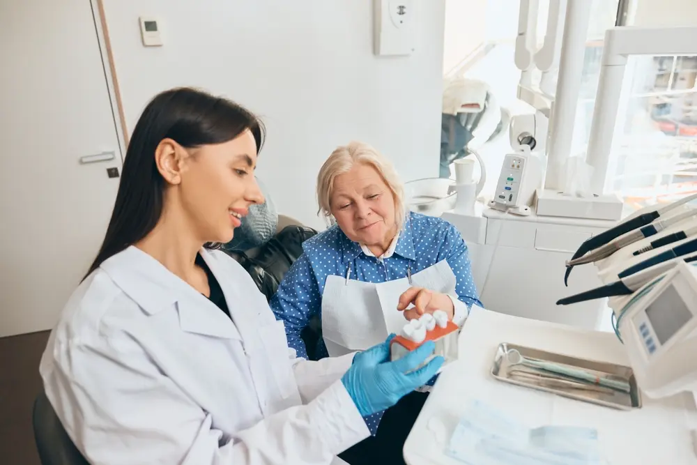 Elderly patient in blue polka-dot blouse consulting with a dentist holding a dental model for implant planning